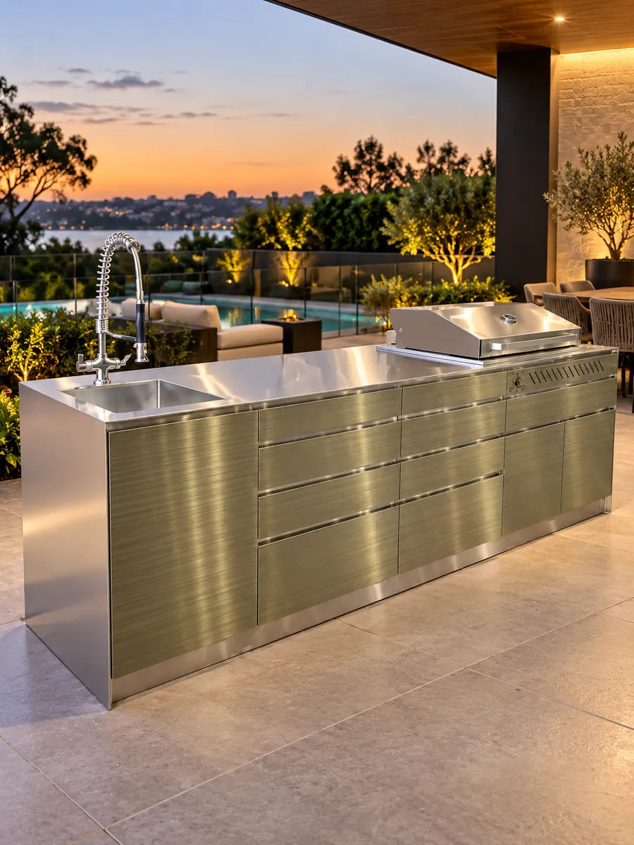 Antique brushed brass outdoor kitchen with built-in BBQ and sink on a terrace at sunset